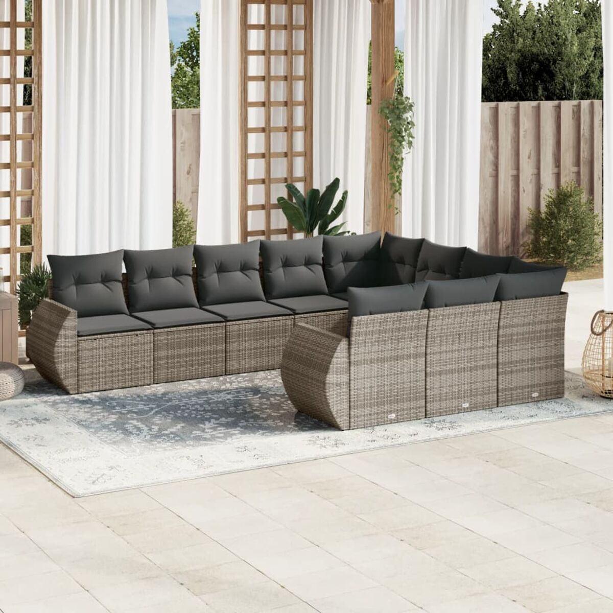 Graues Korbsessel-Sofa mit grauen Kissen auf einem Teppich. Weiße Vorhänge und Holzstruktur im Hintergrund.