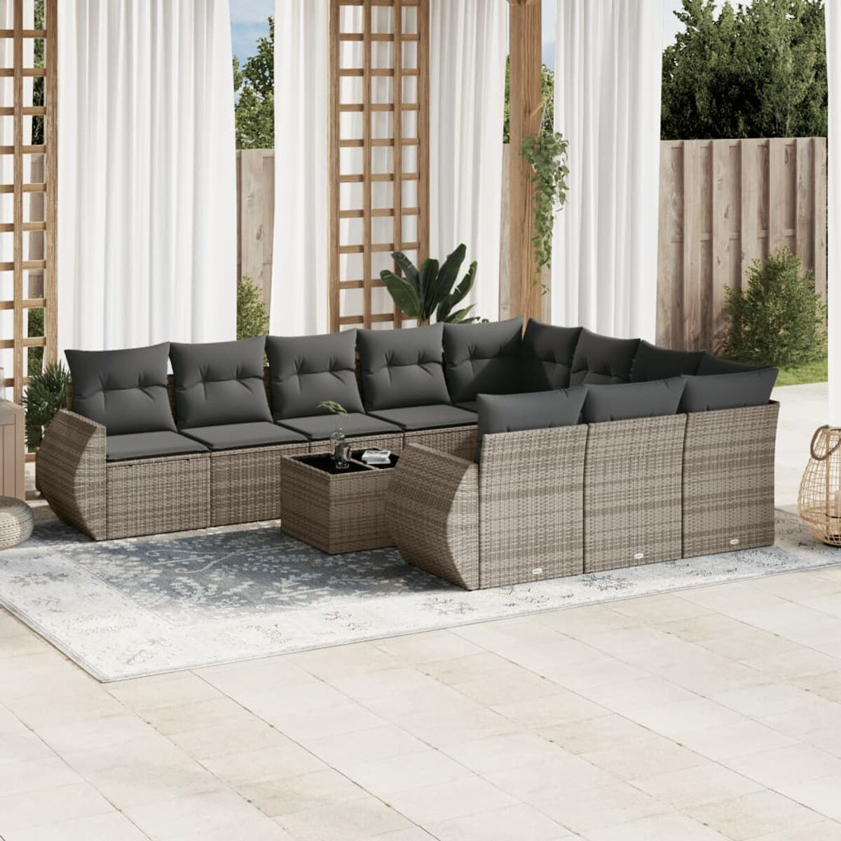 Outdoor-Ecksofa mit grauen Kissen, auf einem Teppich und einem Couchtisch. Weiße Vorhänge und Grün im Hintergrund.
