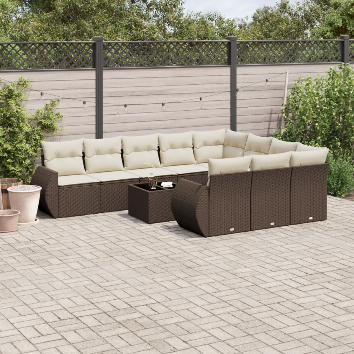 Un divano componibile marrone per esterni con cuscini beige, su un patio in mattoni. Sfondo verde.