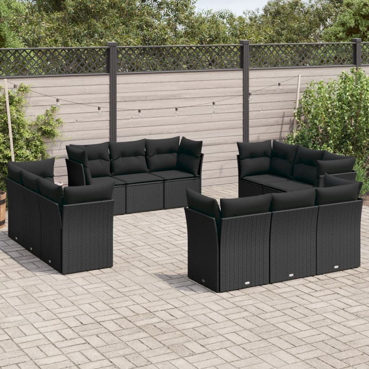 Schwarzes Outdoor-Sofaset. Auf einer Ziegelterrasse angeordnet. Hintergrund mit Zaun und Grün.