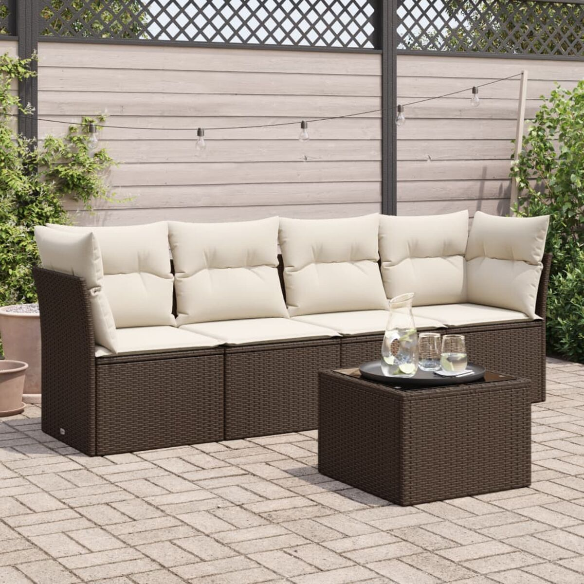 Set divano e tavolo da esterno in vimini marrone con cuscini beige su un patio.