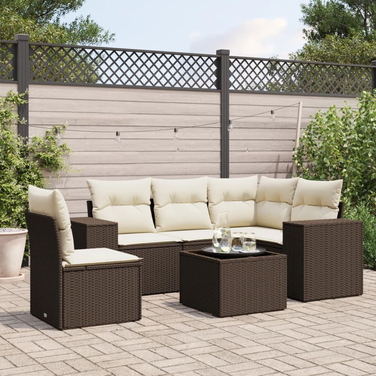 Set divano da esterno, vimini marrone con cuscini color crema, tavolo quadrato e recinzione.