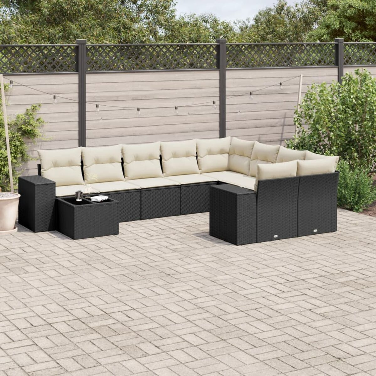 Schwarzes Rattan-Ecksofa mit beigen Kissen auf einer Backstein-Terrasse, mit einem schwarzen Tisch.