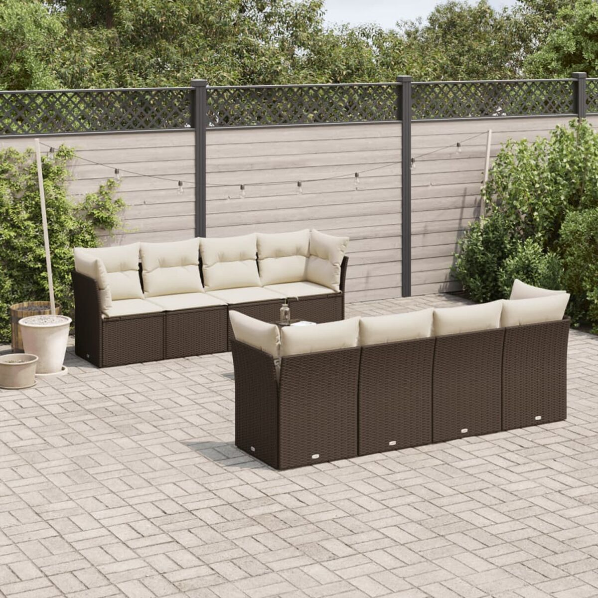 Set di divani in rattan per esterni con cuscini color crema e recinzione in legno.