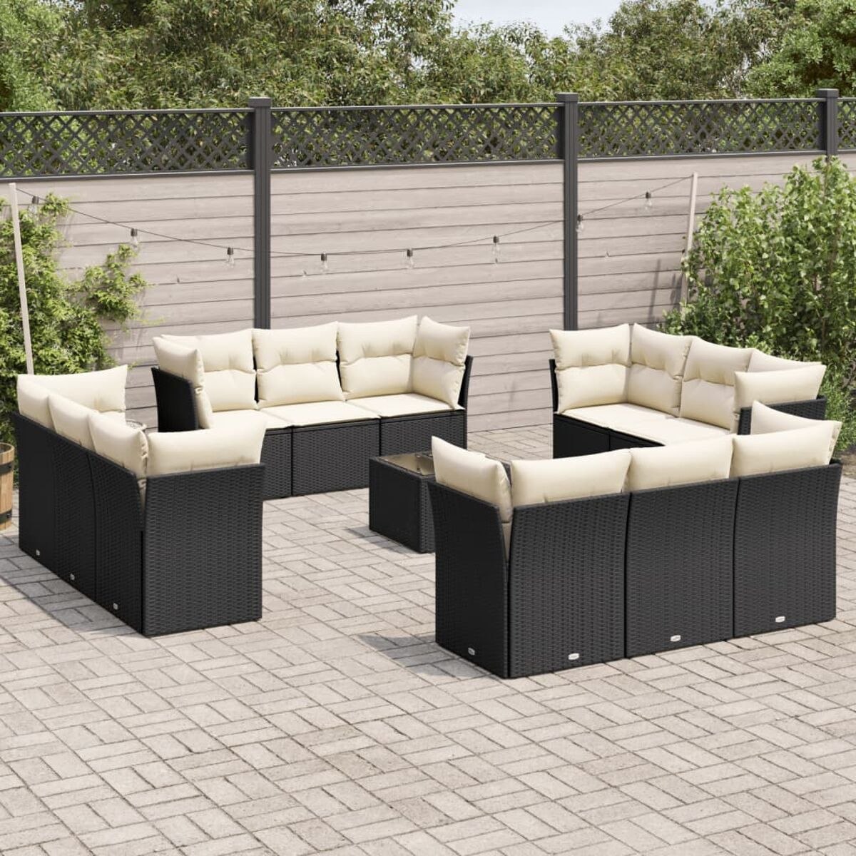 Schwarzes Rattan-Sofa-Set mit beigen Kissen und Glastisch. Ziegel-Terrasse, Zaun und Pflanzen.
