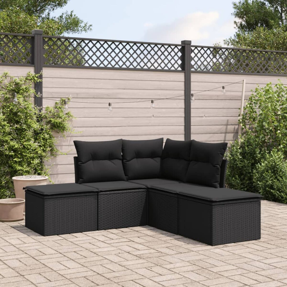 Schwarzes Outdoor-Ecksofa aus Korbgeflecht mit schwarzen Kissen auf einer Ziegelterrasse. Zaun im Hintergrund.