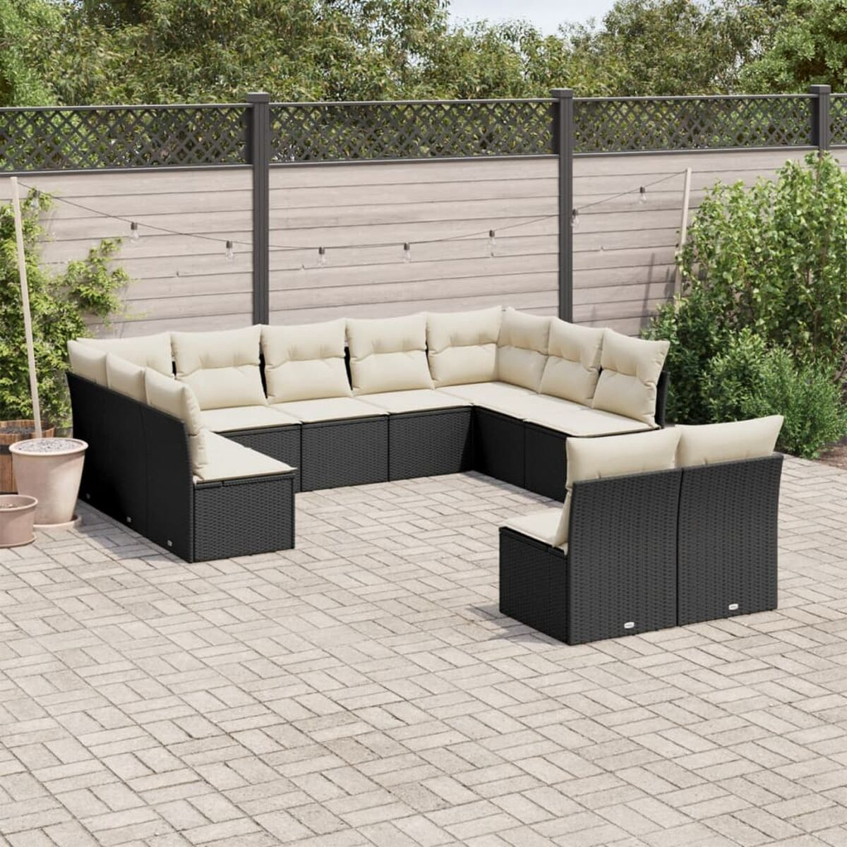 Schwarzes Outdoor-Ecksofa aus Korbgeflecht mit beigen Kissen auf Ziegelpflaster, Holzzaun.