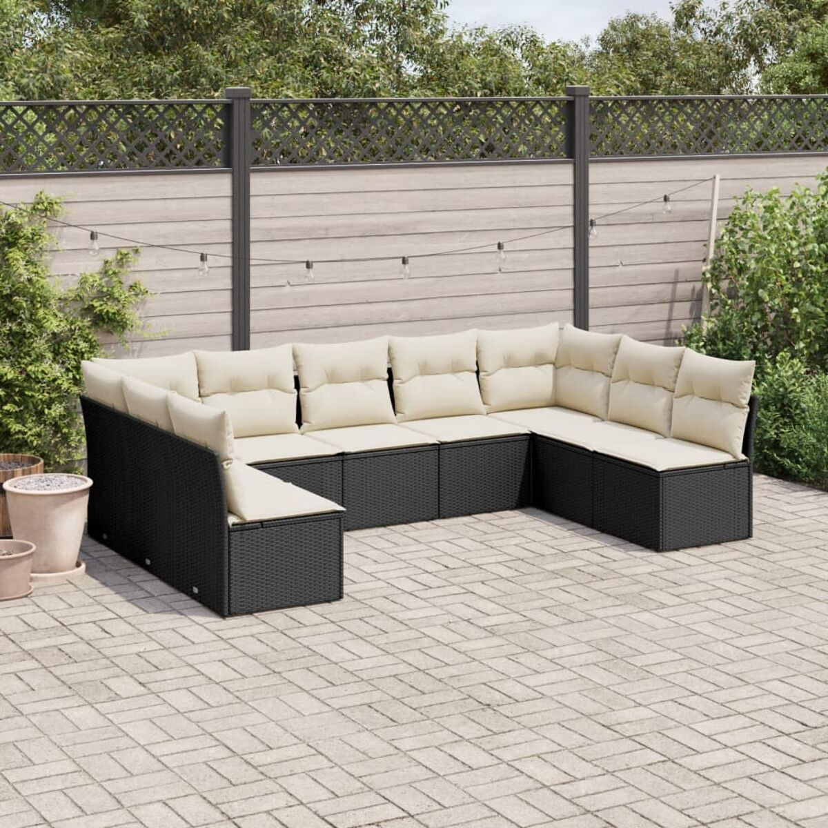Schwarzes Ecksofa aus Korbgeflecht mit cremefarbenen Kissen auf einer Ziegelterrasse, in der Nähe von Pflanzen.