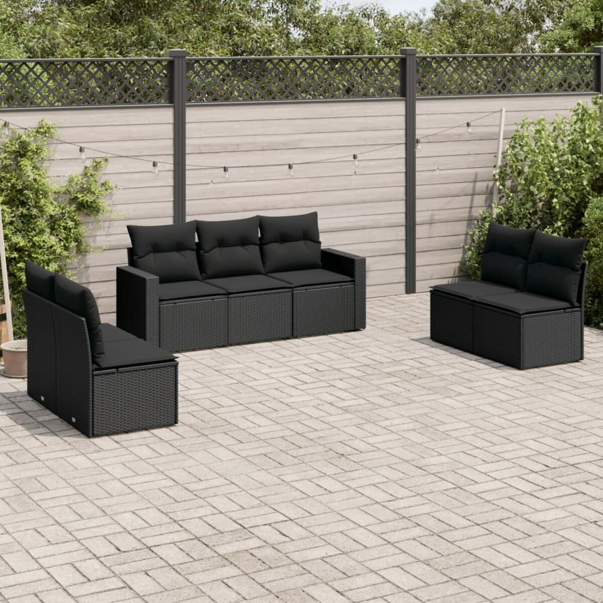 Rattan-Outdoor-Sofagarnitur mit schwarzen Kissen. Auf einer Ziegelterrasse vor einem Zaun.