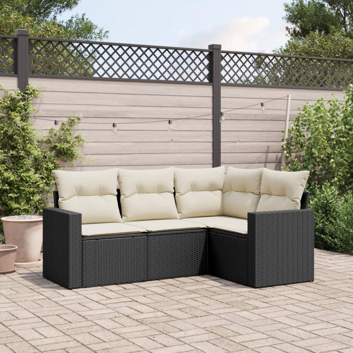 Schwarzes Korbsessel-Ecksofa mit cremefarbenen Kissen auf einer Ziegelterrasse. HolzZaun und Pflanzen im Hintergrund.