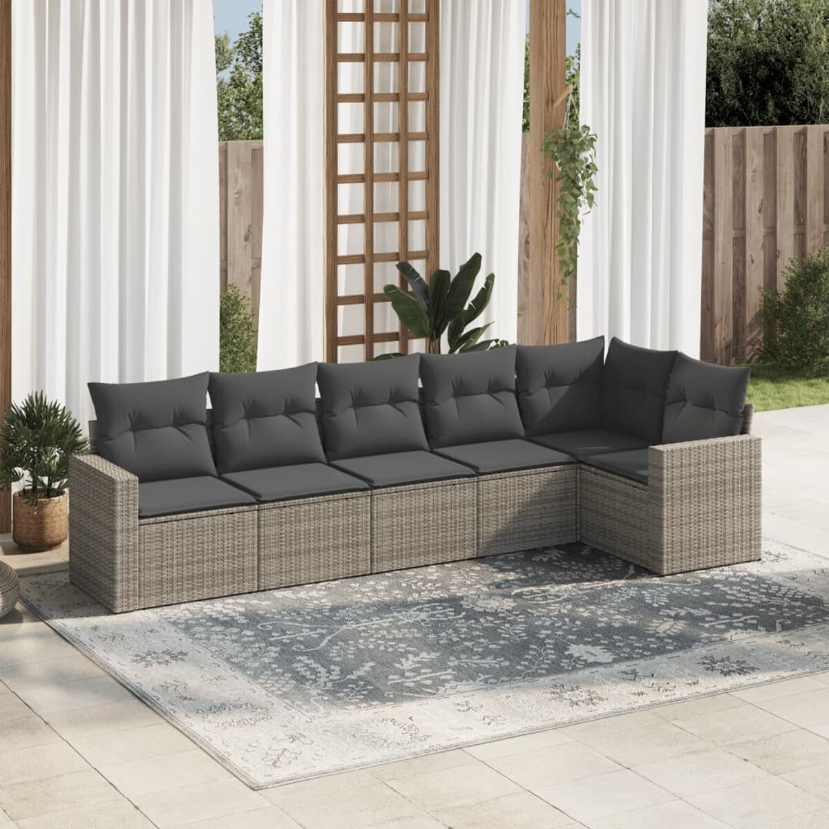 Rattan-Sofagarnitur mit grauen Kissen, Vorhängen und einem Teppich.