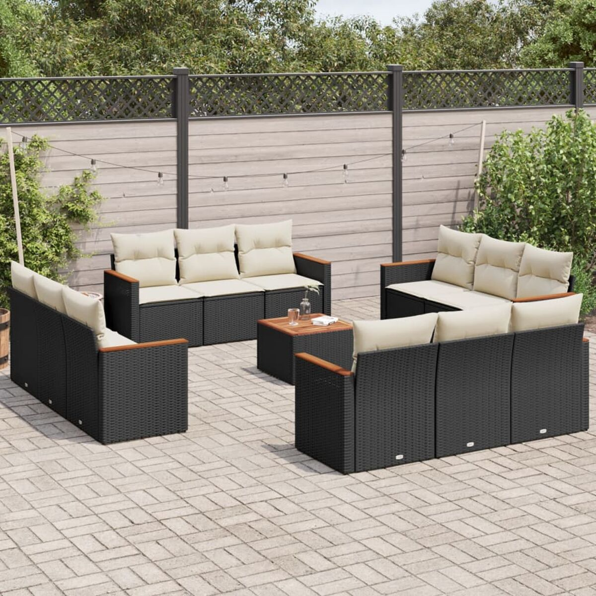 Schwarzes Outdoor-Möbelset aus Korbgeflecht mit beigefarbenen Kissen auf einer Ziegelterrasse und einem Zaun.
