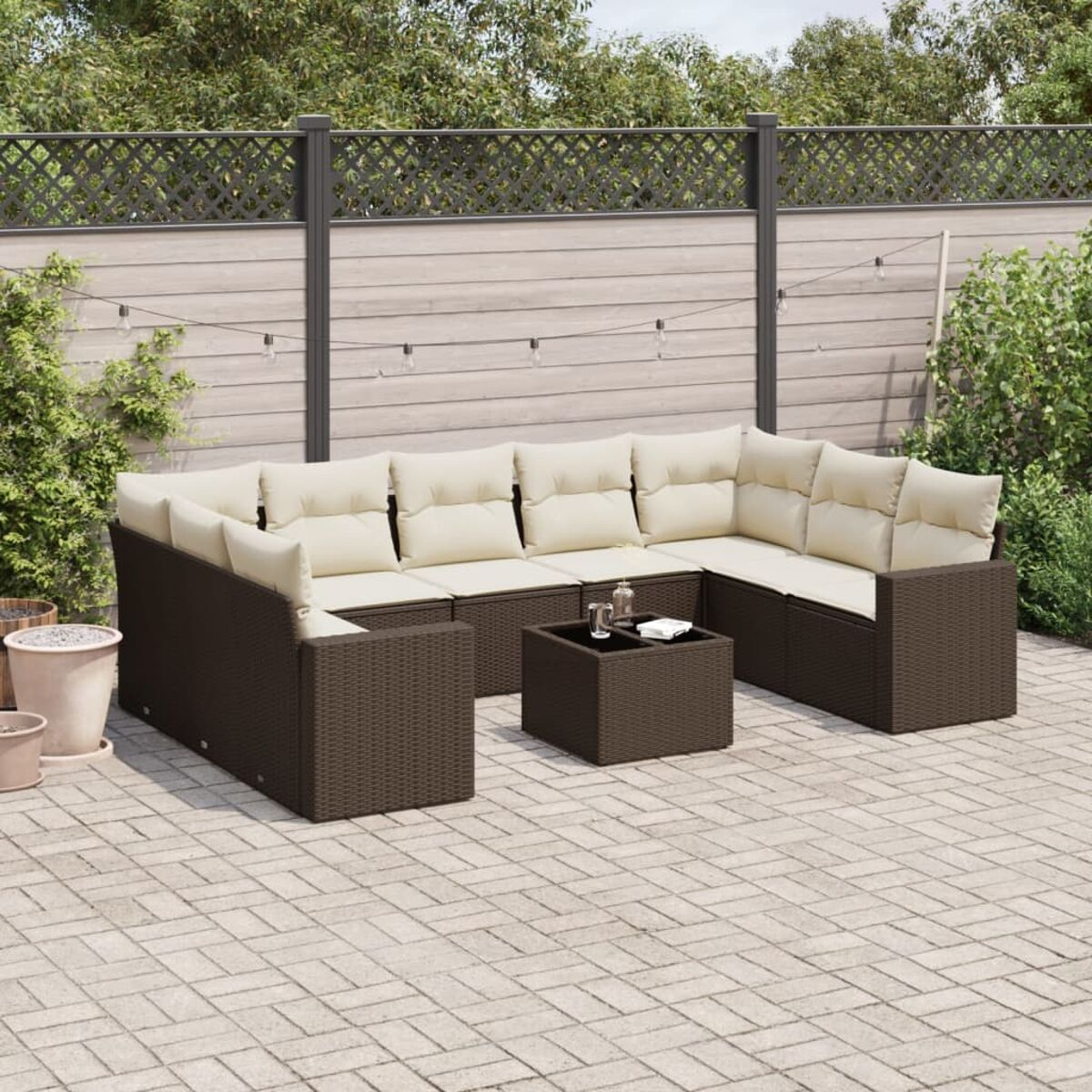 Set divano in rattan da esterno con cuscini beige, tavolo e sfondo giardino.