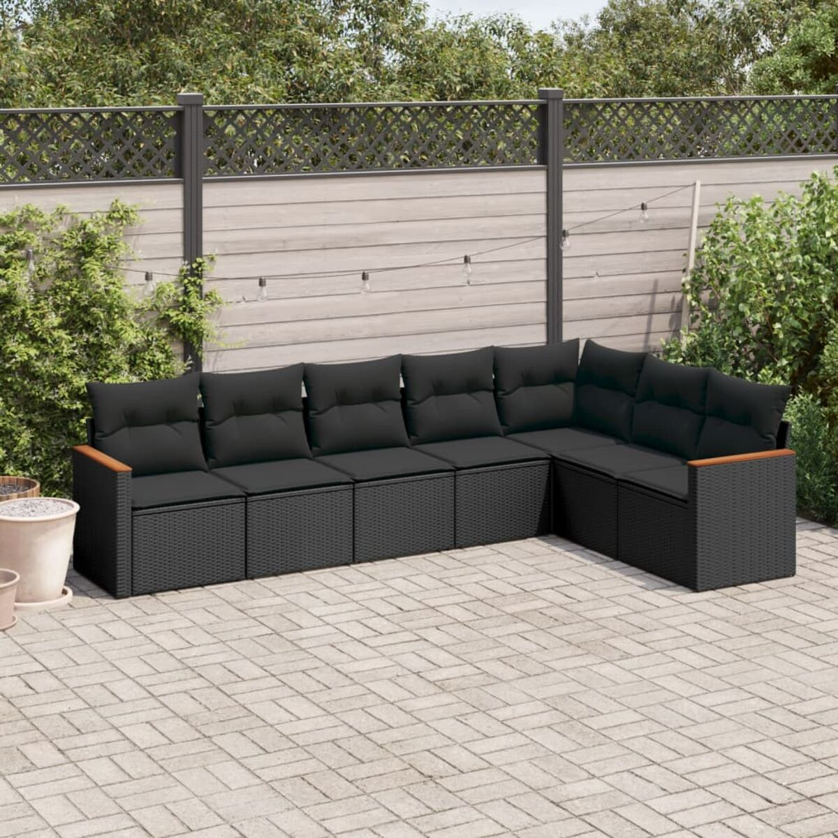 Schwarzes L-förmiges Sofa mit schwarzen Kissen auf einer Backstein-Terrasse im Garten.