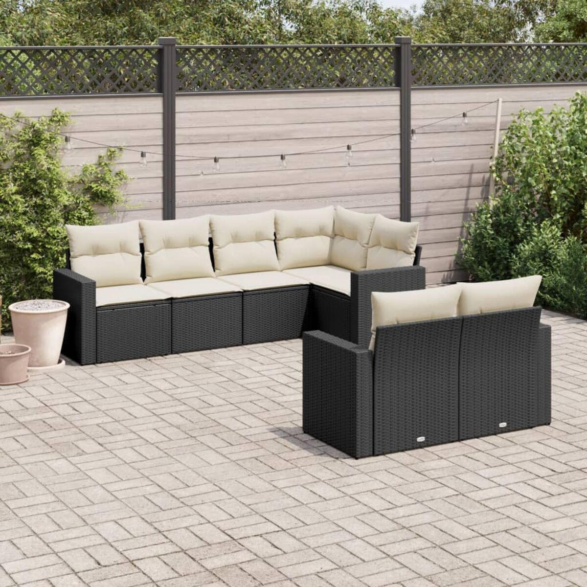 Schwarzes Ecksofa-Set mit beigen Kissen auf Ziegelterrasse mit Holzzaun und Pflanzen im Hintergrund.