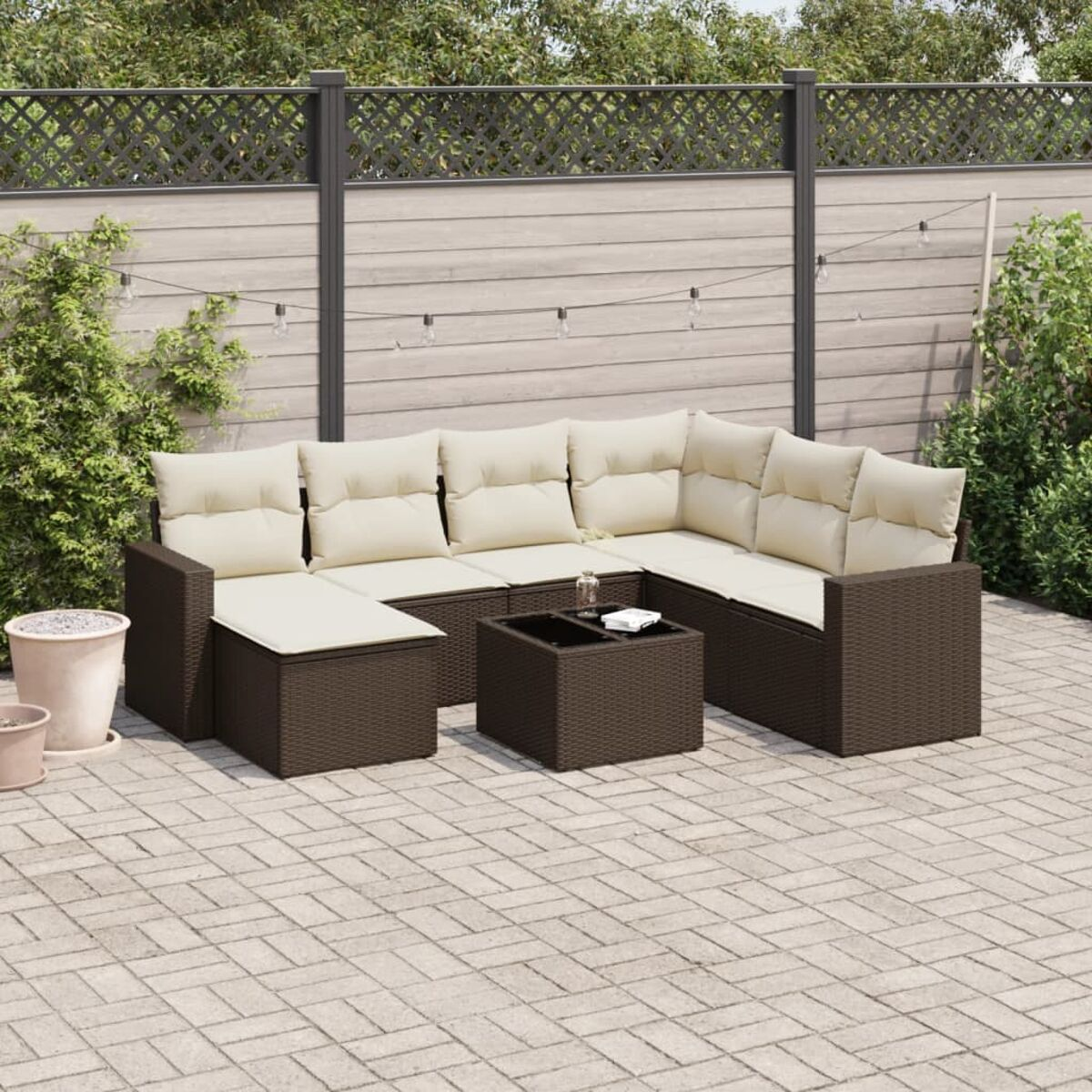 Divano componibile in vimini marrone con cuscini color crema e tavolino su un patio.