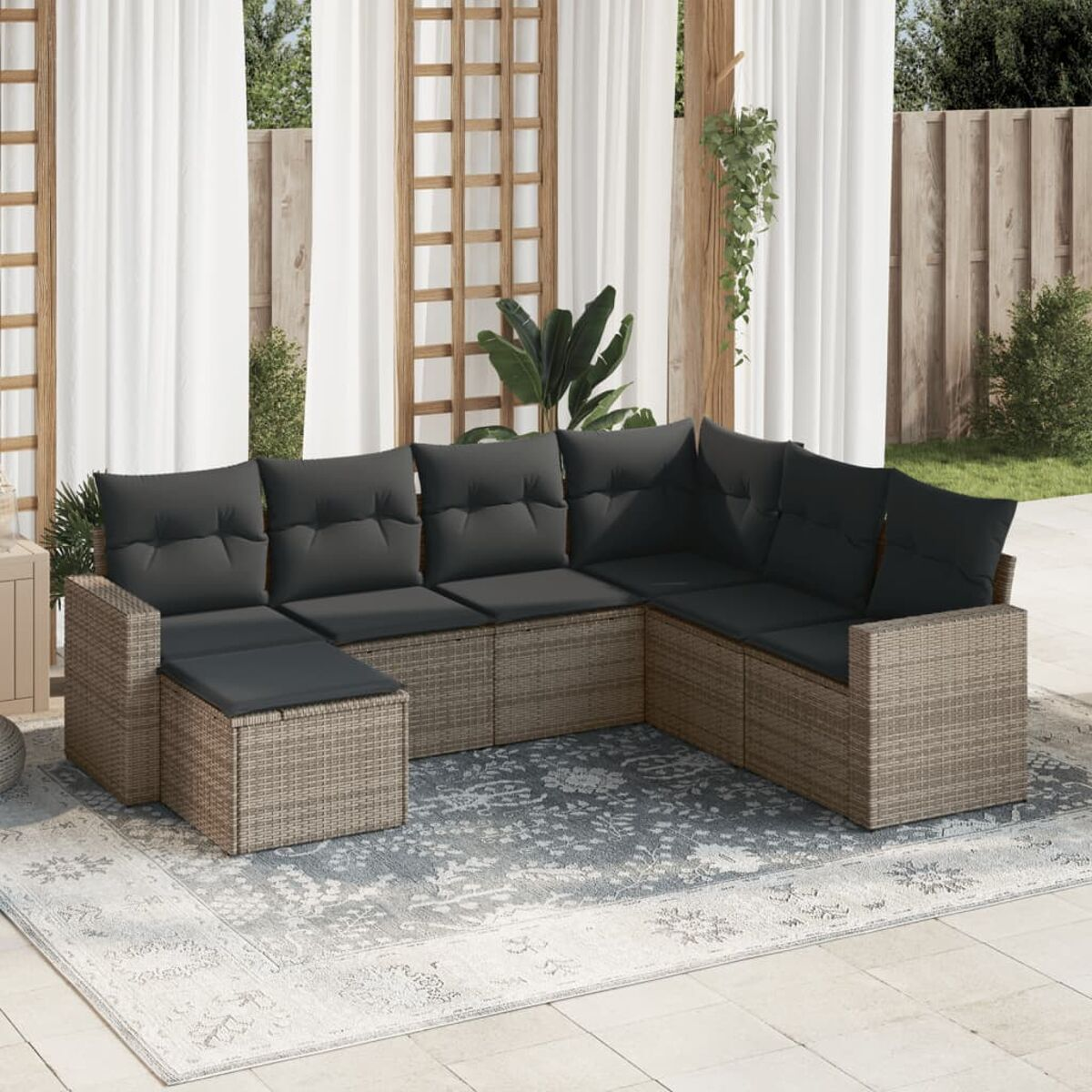 Outdoor-Ecksofa aus Korbgeflecht mit grauen Kissen auf einem gemusterten Teppich.