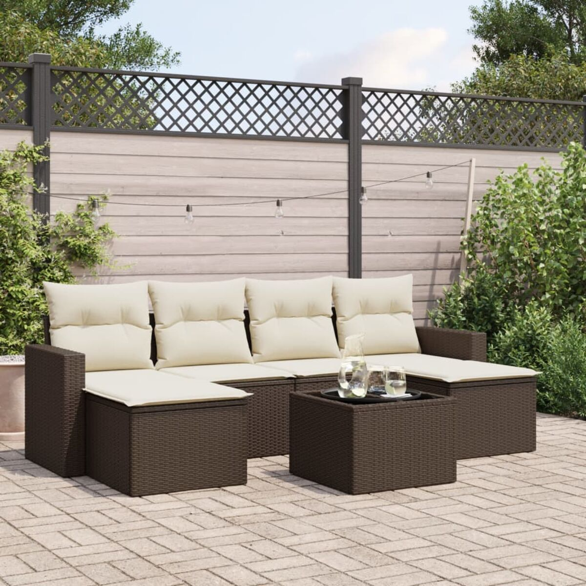 Un set di divani marroni intrecciati per esterni con cuscini color crema, su un patio in mattoni, con sfondo di recinzione.