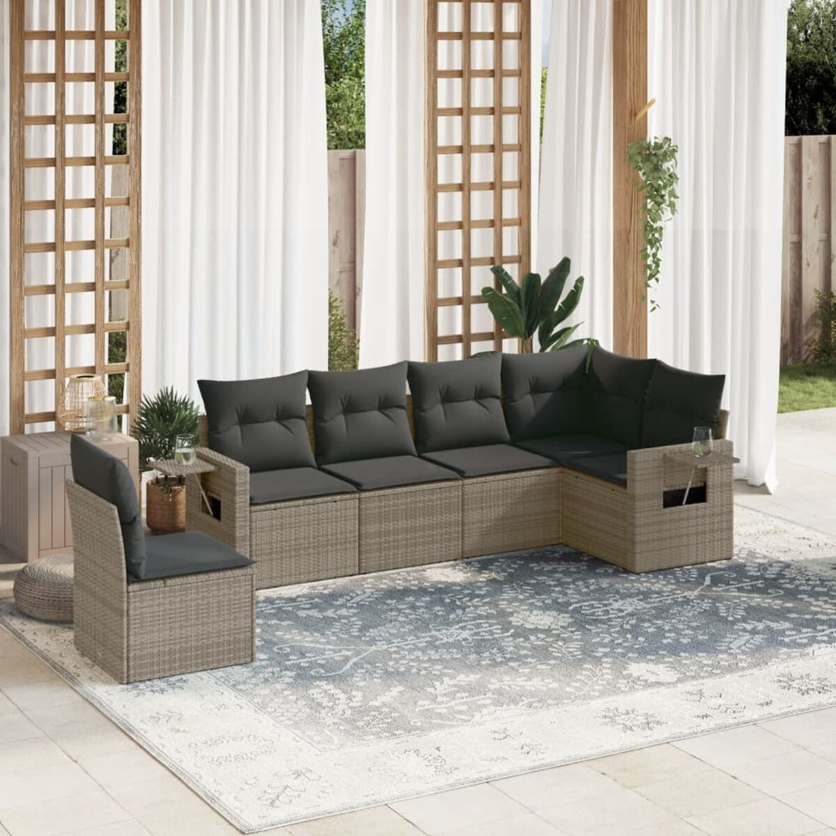 Ein graues Outdoor-Sofaset aus Rattan wird auf einem Teppich mit weißen Vorhängen im Hintergrund gezeigt.