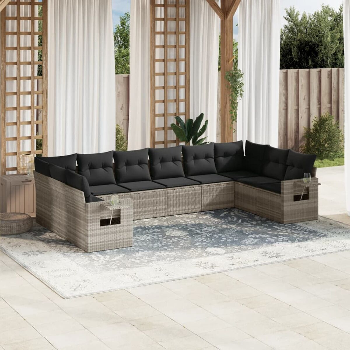 Rattan-Outdoor-Sofagarnitur mit schwarzen Kissen. Die Szene ist im Freien mit weißen Vorhängen und einem Teppich.