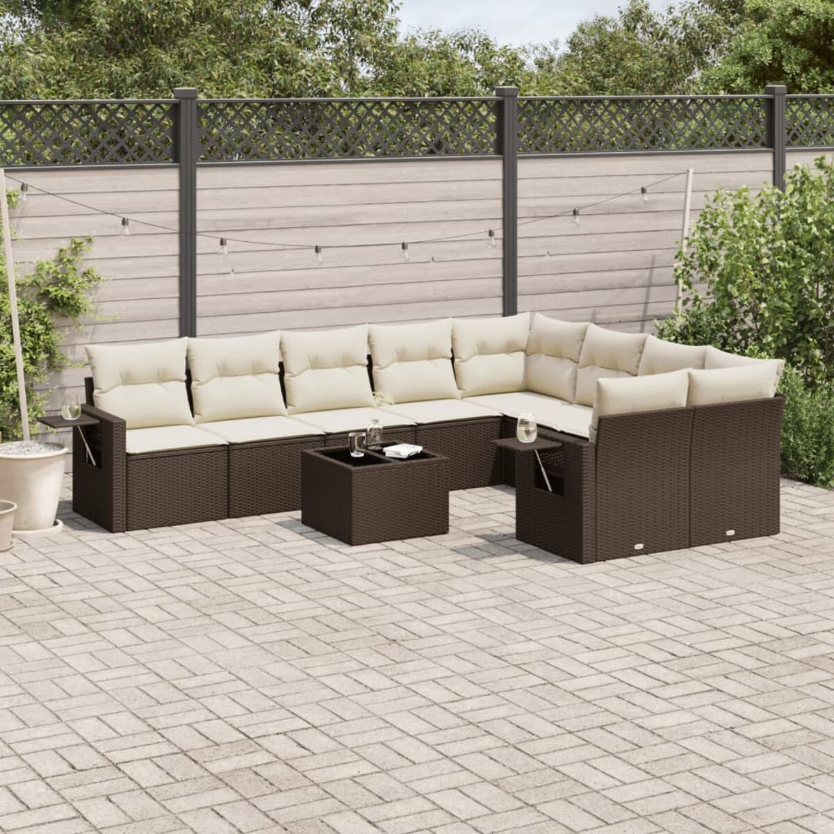 Divano in vimini marrone scuro con cuscini color crema. Patio in mattoni e recinzione in legno sullo sfondo.