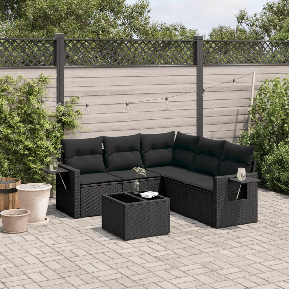 Schwarzes Korbsessel-Gartensofa mit Tisch auf einer Backstein-Terrasse. Inklusive Gläser und Blumen.