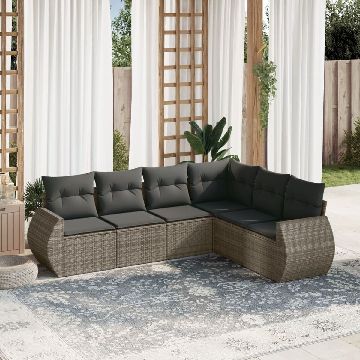 Graues Ecksofa für den Außenbereich mit dunkelgrauen Kissen, auf einem Teppich, mit weißen Vorhängen im Hintergrund.
