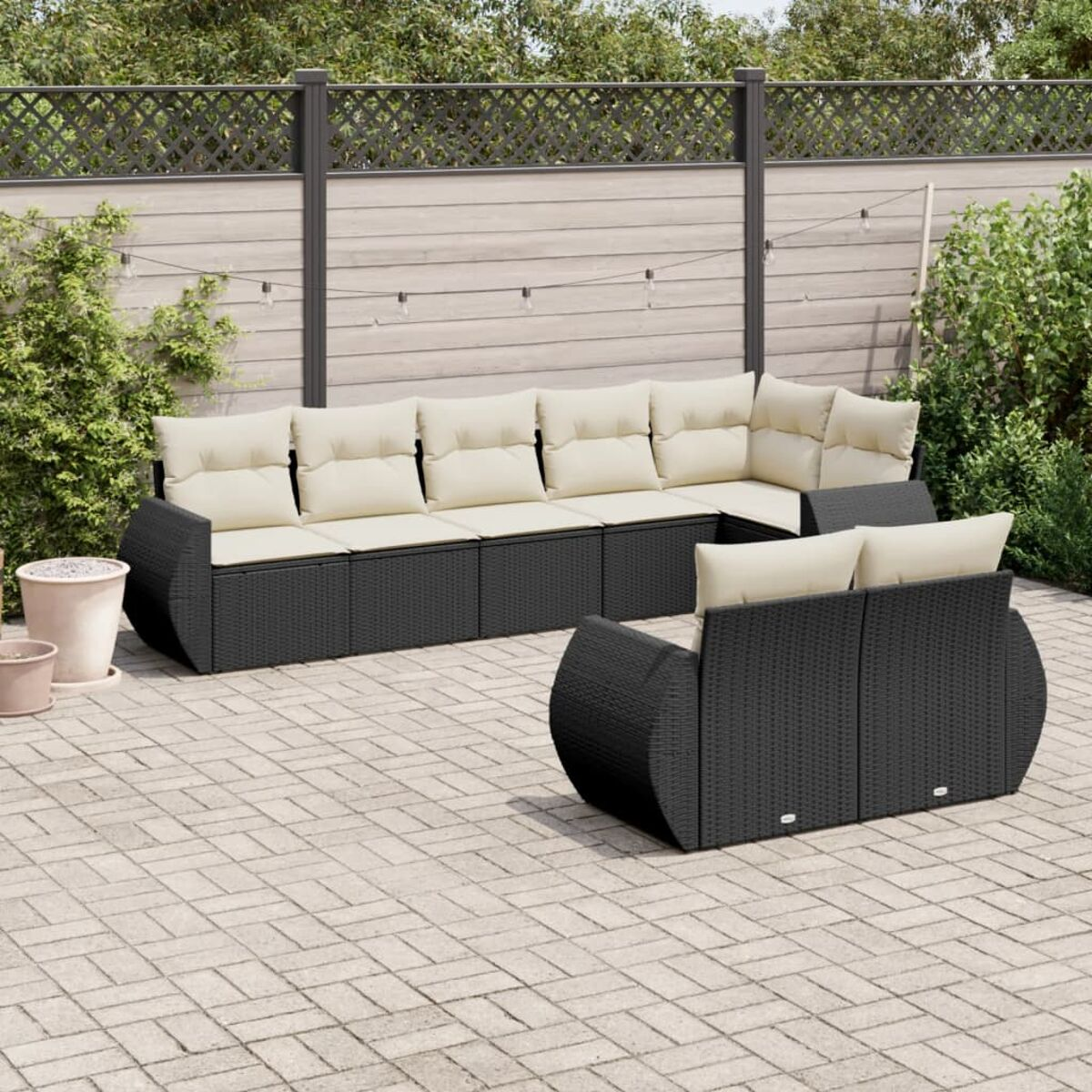 Ein Terrassenset mit schwarzen Korbmöbeln auf einer Ziegelterrasse mit Holzzaun im Hintergrund.