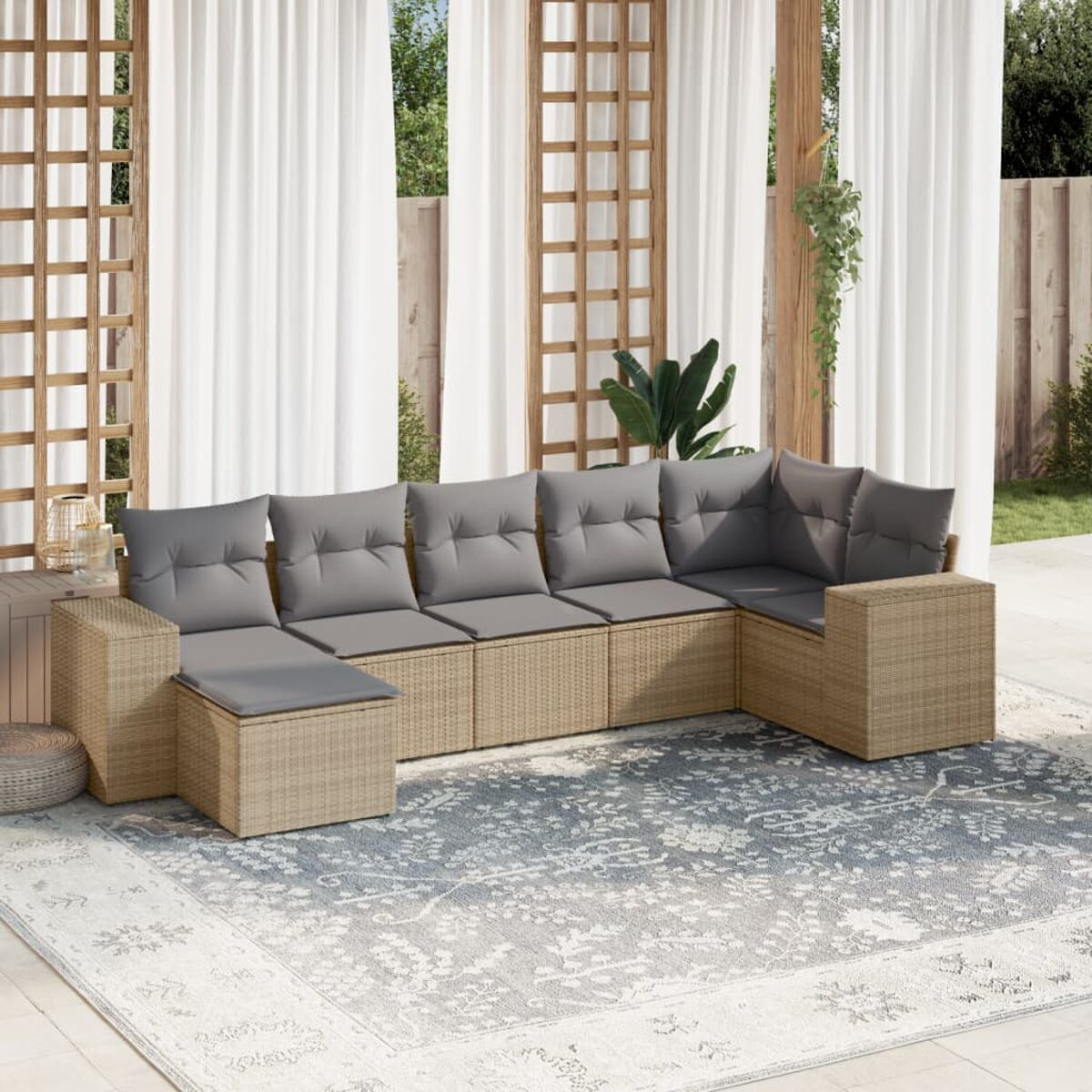 Garten-Ecksofa mit grauen Kissen auf einem Teppich, in der Nähe weißer Vorhänge, mit Grün im Hintergrund.