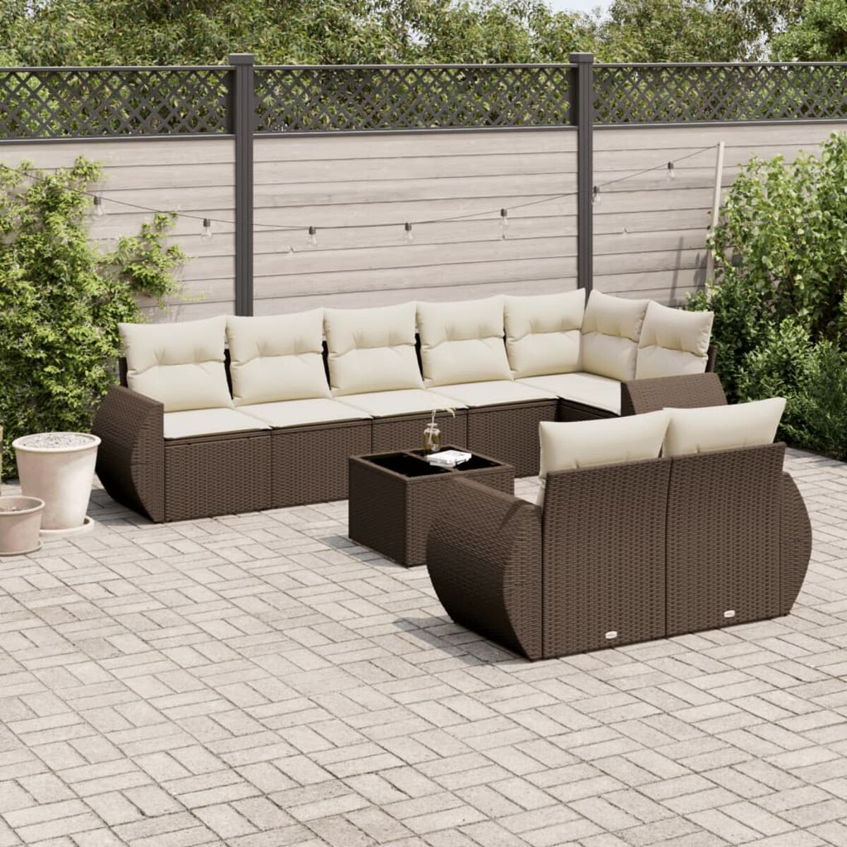 Set divano componibile da esterno in rattan marrone con tavolino quadrato su un patio in mattoni, con piante e recinzione.