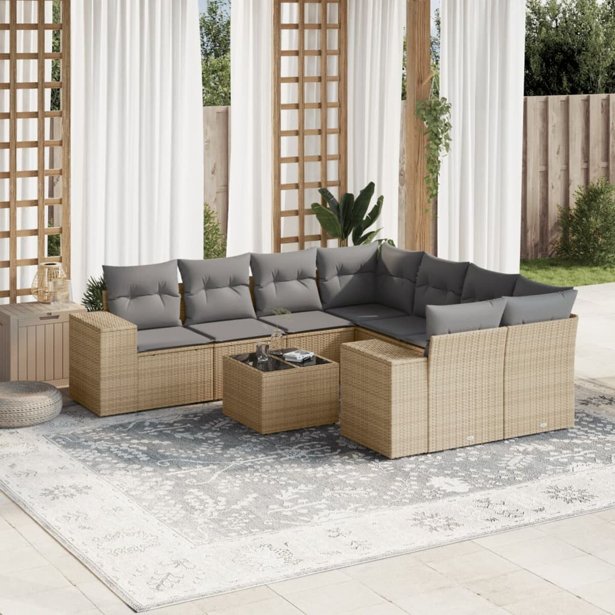Beiges Ecksofa aus Korbgeflecht mit grauen Kissen, einem Tisch, auf einem gemusterten Teppich, unter einer Holzkonstruktion, mit Vorhängen.