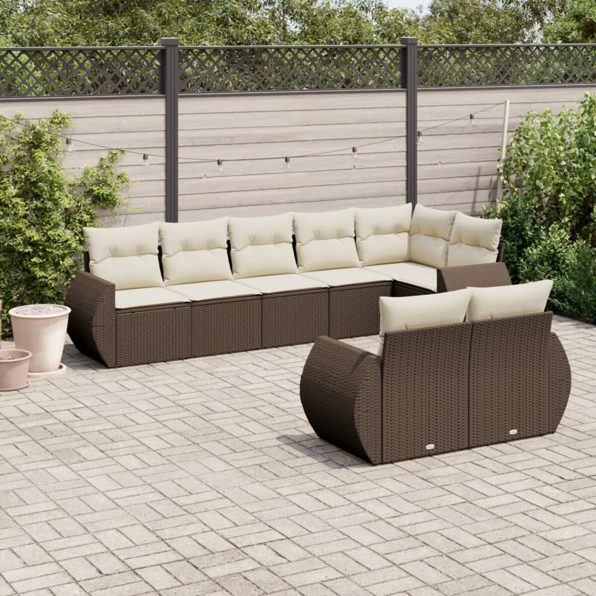 Set patio con divano componibile in vimini marrone e due sedie. Cuscini beige. Pavimento lastricato.