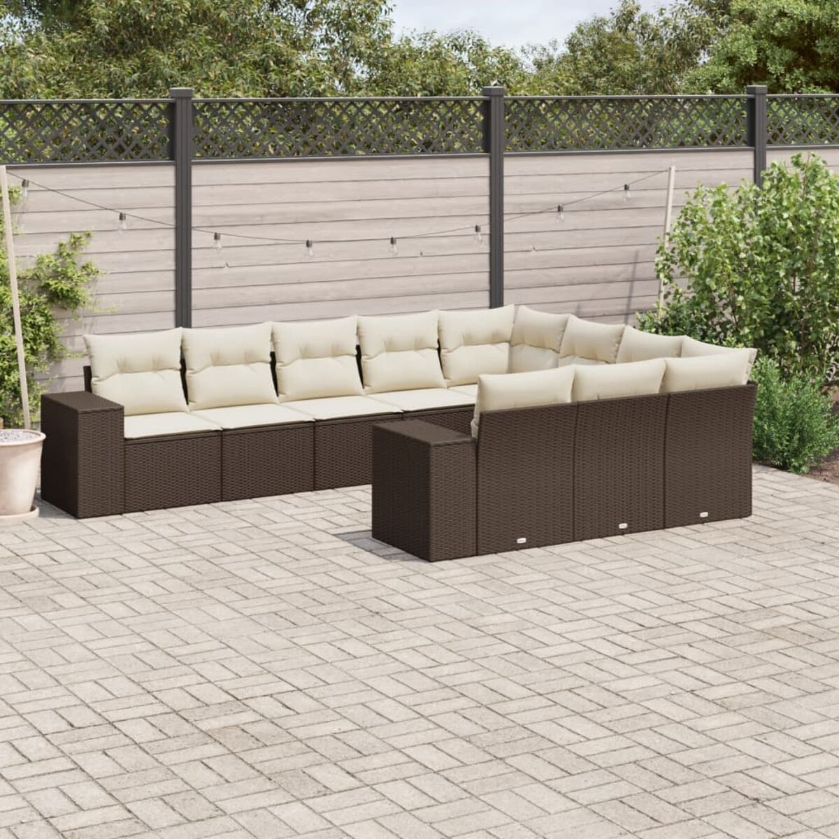 Divano componibile da esterno in rattan marrone con cuscini color crema su un patio in mattoni.