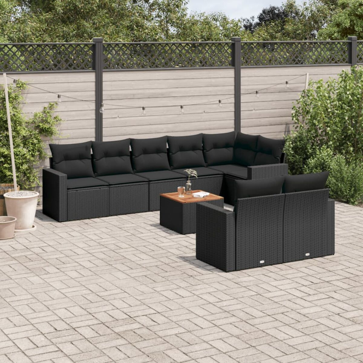 Schwarzes Outdoor-Ecksofa aus Korbgeflecht mit schwarzen Kissen und kleinem Tisch. Terrasse mit Zaun.