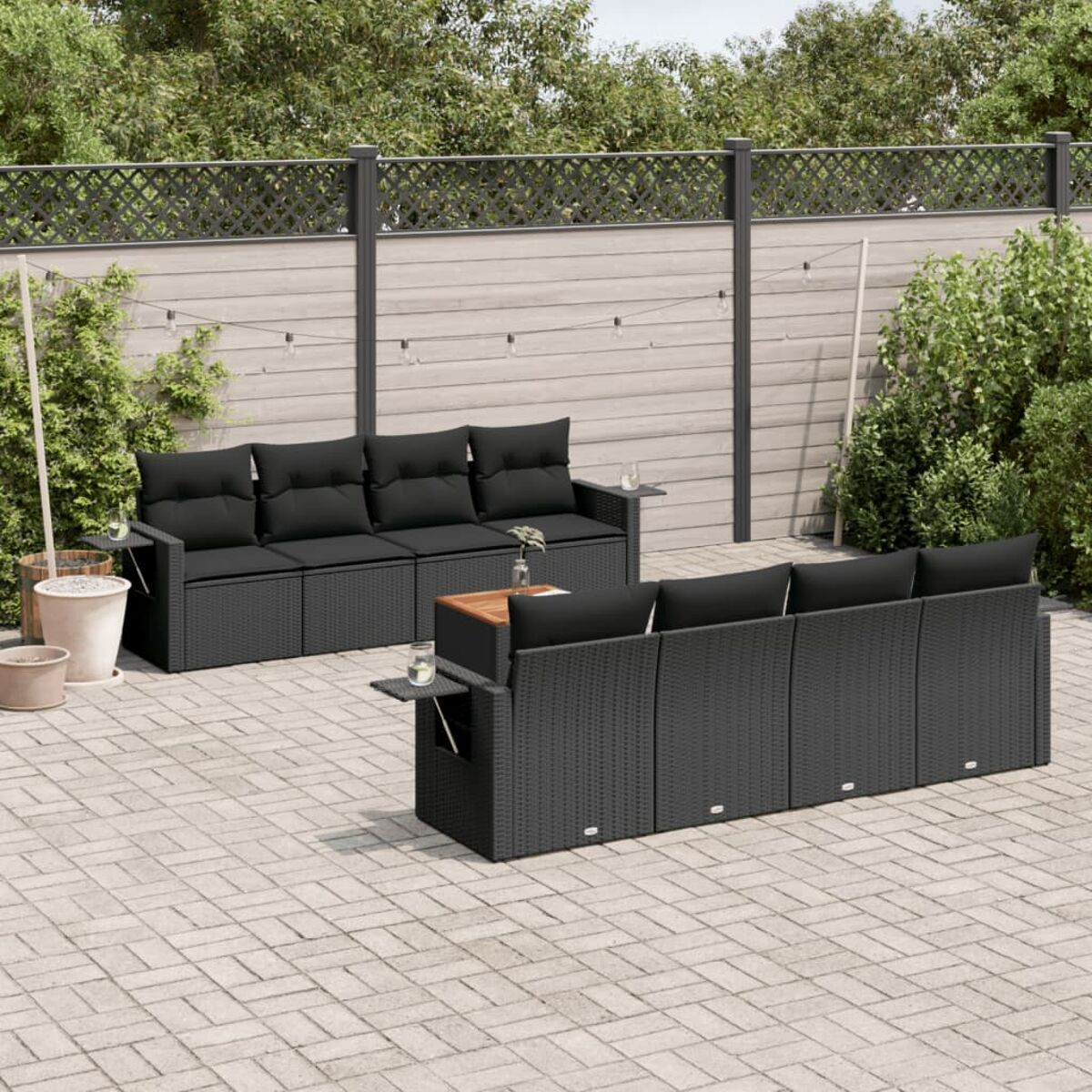 Zwei schwarze Rattansofas mit schwarzen Kissen stehen auf einer gepflasterten Terrasse. Es gibt kleine Beistelltische.