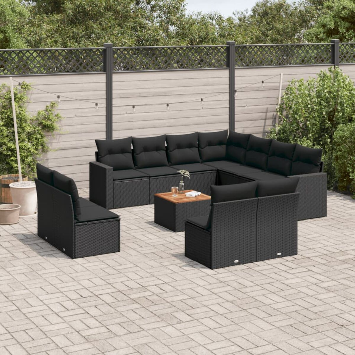 Schwarzes Outdoor-Möbelset aus Korbgeflecht auf einer Terrasse, inklusive Sofa, Stühlen und Tisch.