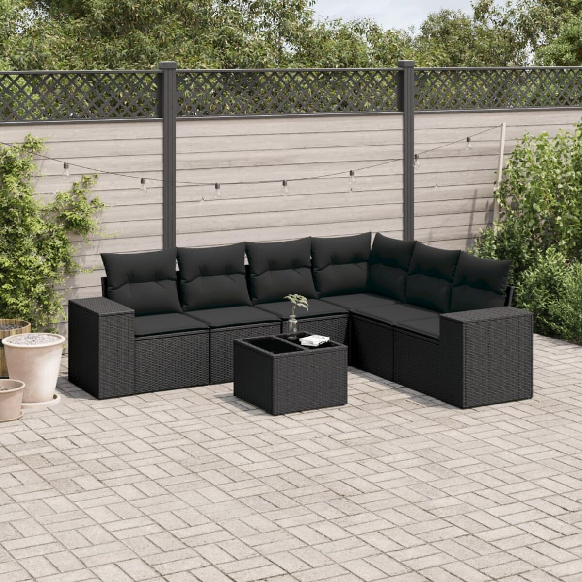 Schwarzes Rattan-Ecksofa mit schwarzen Kissen und einem Couchtisch auf einer Terrasse.