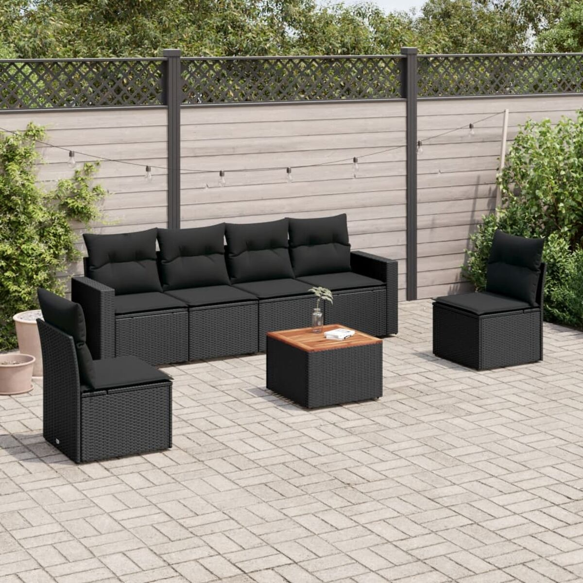 Garten-Set: schwarzes Sofa, zwei Stühle und ein Tisch. Schwarze Kissen und gepflasterte Terrasse.