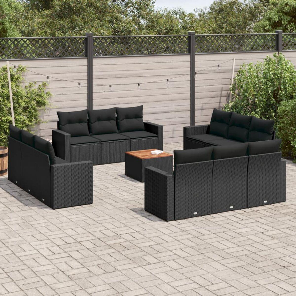 Outdoor-Sofagarnitur aus schwarzem Korbgeflecht. Holztisch. Ziegelterrasse, grüne Pflanzen, Holzzaun.
