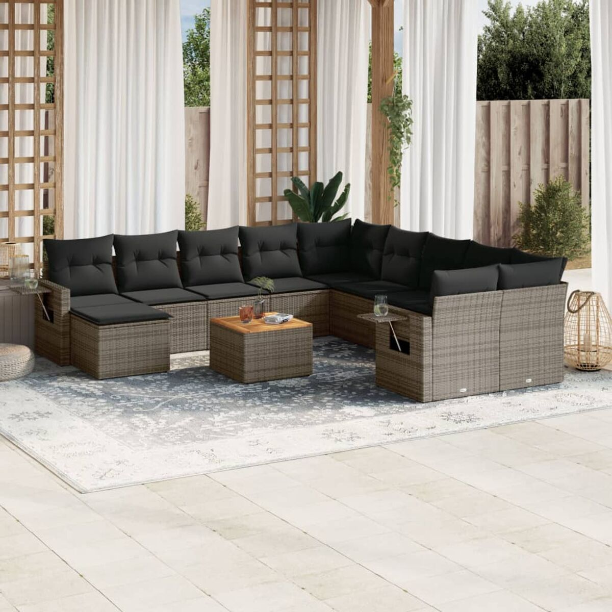 Outdoor-Terrassenset, Korbmöbel mit schwarzen Kissen, einem Couchtisch und einem Teppich. Weiße Vorhänge.