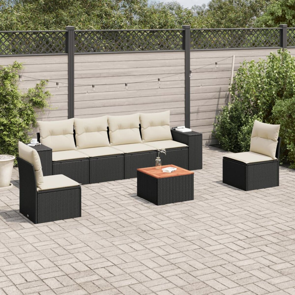 Set da patio in vimini nero con cuscini color crema. Include divano, due sedie e un tavolino.