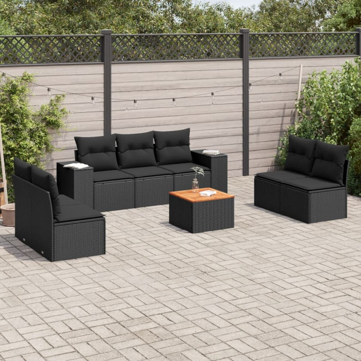 Schwarzes Outdoor-Möbelset aus Korbgeflecht mit schwarzen Kissen und einem quadratischen Tisch auf einer Backstein-Terrasse.