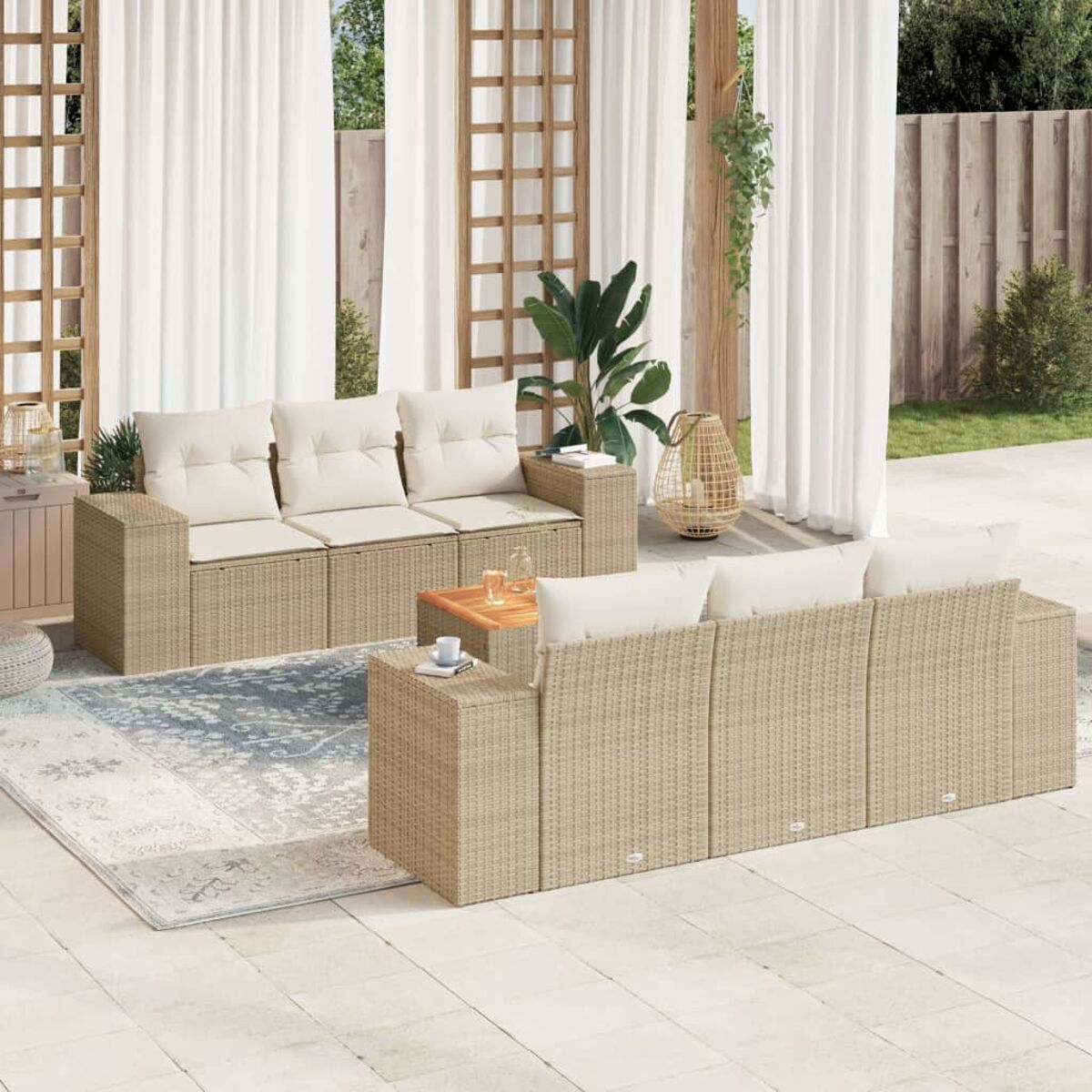 Beiges Outdoor-Sofa-Set aus Korbgeflecht mit cremefarbenen Kissen, Holztisch, auf einem Teppich. Weiße Vorhänge und grüne Pflanzen.