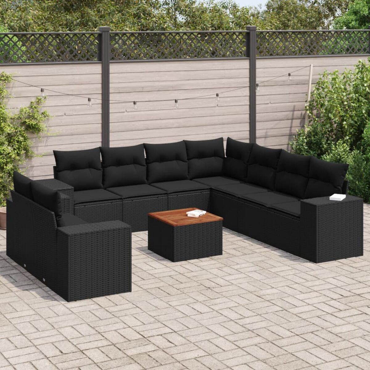 Schwarzes Outdoor-Ecksofa aus Korbgeflecht mit schwarzen Kissen, Couchtisch. Terrasse, Zaun, Lichter.