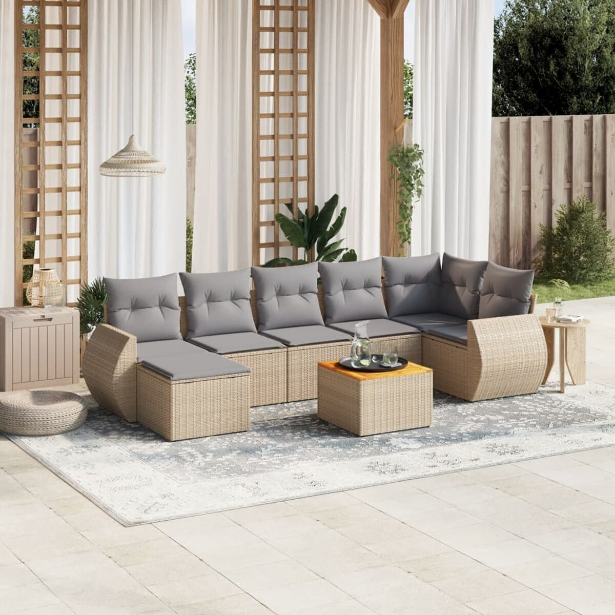 Rattan-Outdoor-Sofa mit grauen Kissen und einem kleinen Tisch. Auf einem gemusterten Teppich, mit Deko.