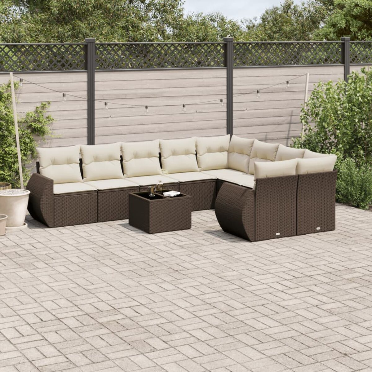 Set divano componibile in rattan marrone con cuscini color crema e tavolino quadrato, su un patio pavimentato.