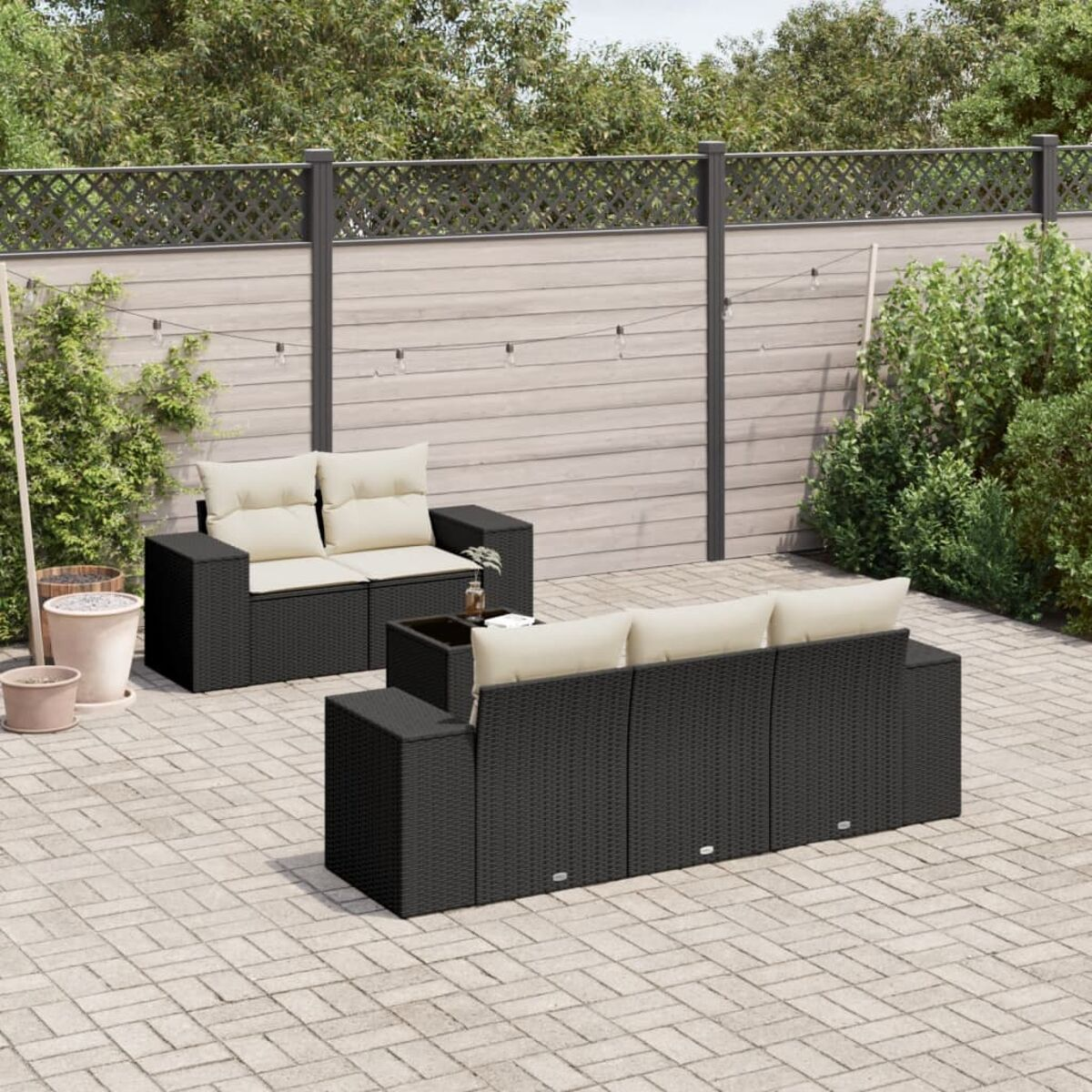 Schwarzes Korbmöbel-Outdoor-Sofa mit cremefarbenen Kissen auf einer Steinterrasse.