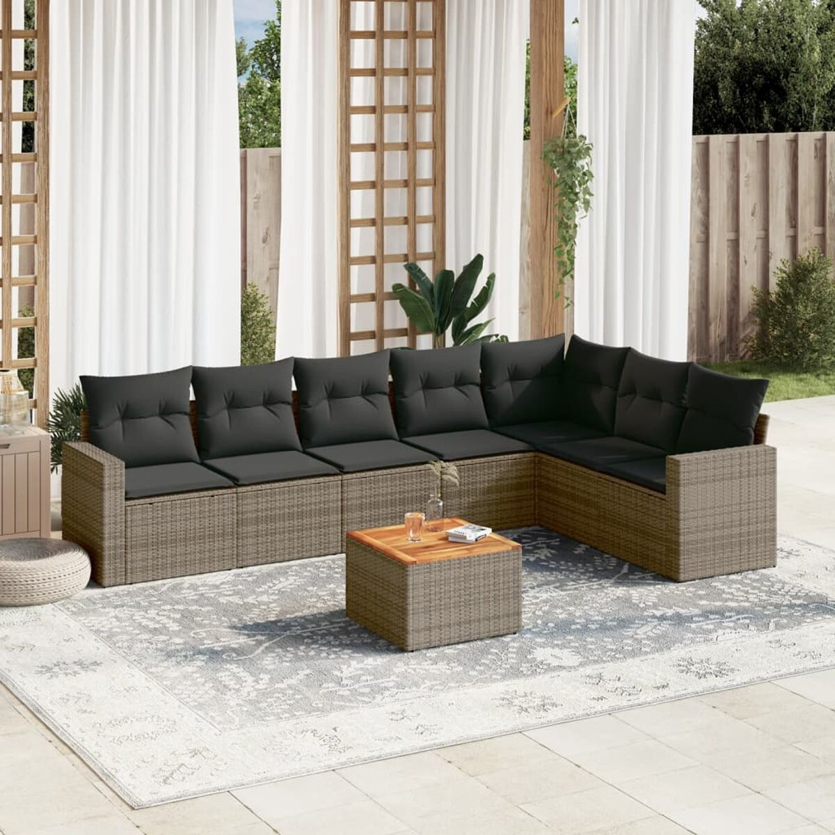 Graues Korbsessel-Sofa mit grauen Kissen und einem Couchtisch auf einem Teppich. Szene in sonniger Umgebung.