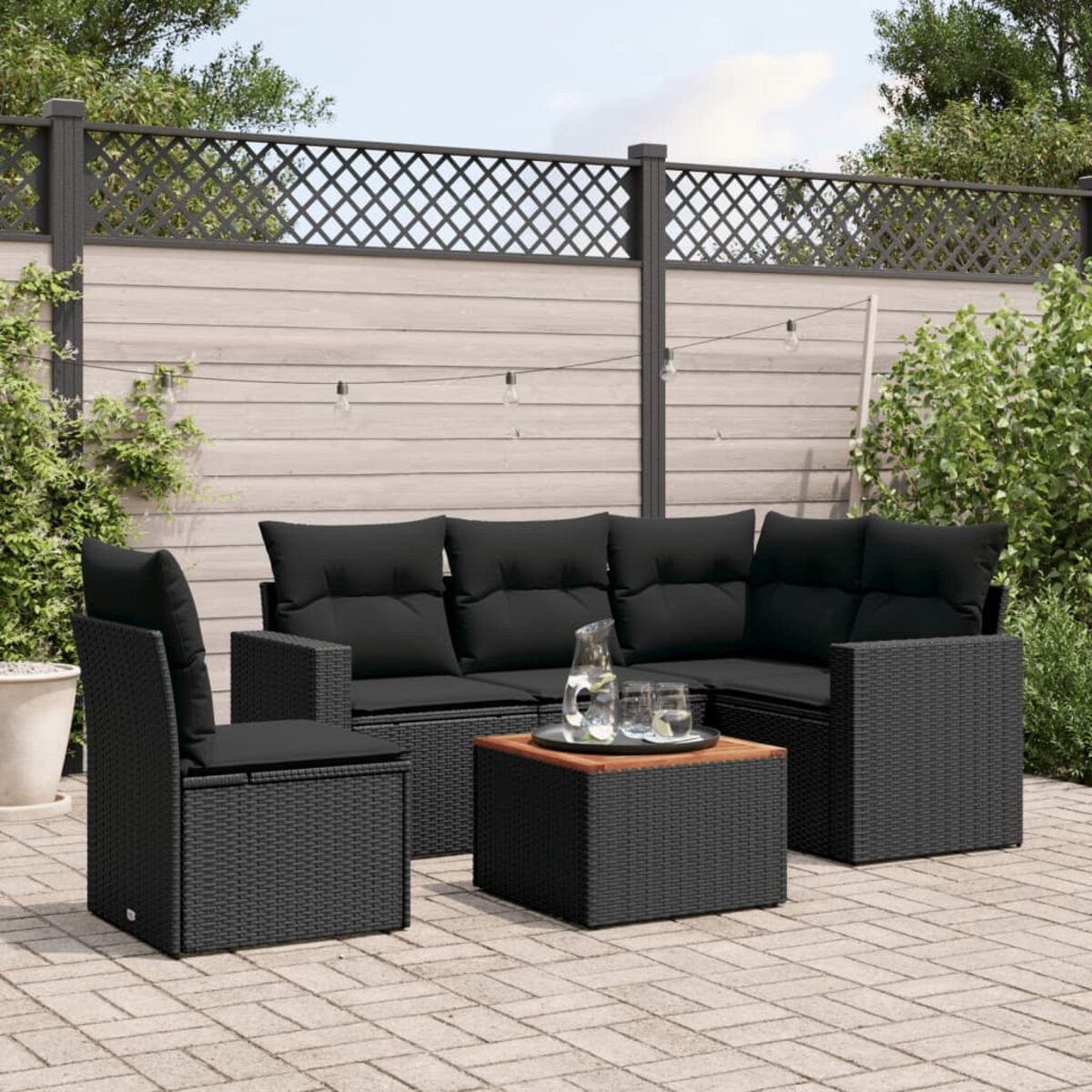 Outdoor-Sitzgruppe: Sofa, zwei Stühle, kleiner Tisch, alles aus schwarzem Korbgeflecht, mit schwarzen Kissen.