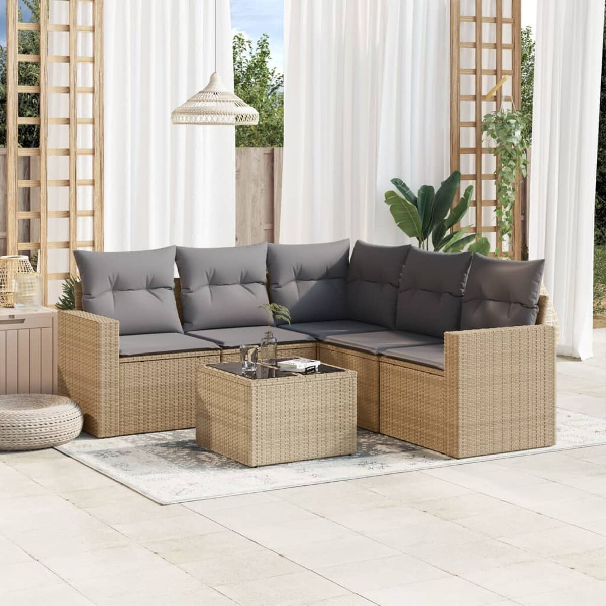 Ecksofa aus Korbgeflecht mit grauen Kissen und Couchtisch auf einem Teppich. Weiße Vorhänge und Hängelampe sichtbar.